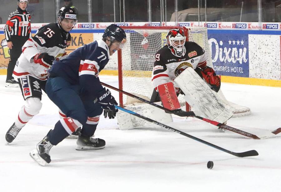 Bek Christián Michalčin (75) a gólman Dominik Hrachovina (obaja Banská Bystrica) sledujú akciu obrancu Slovana Kubku v 14. kole Tipos extraligy 2024/2025 v zápase HC ′05 Banská Bystrica proti HC Slovan Bratislava